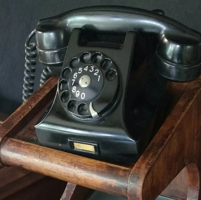 telefone antigo de disco preto, material baquelite, sobre móvel de madeira