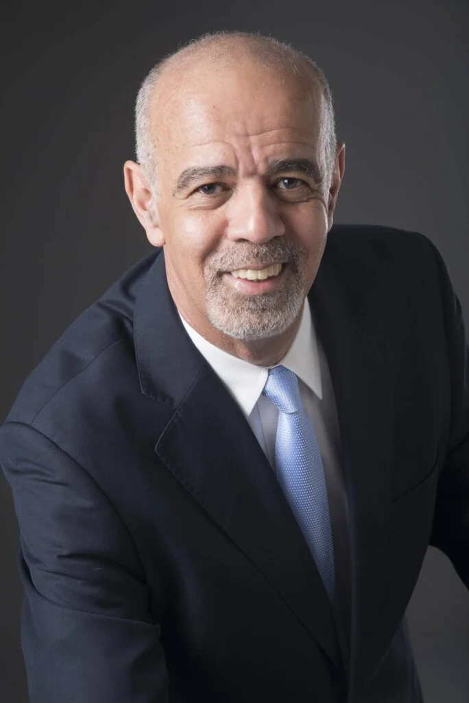 retrato profissional de homem de meia idade,sorrindo, com terno escuro e gravata azul, com luz dramática e fundo escuro