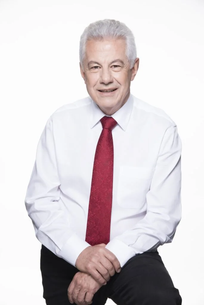 retrato profissional de homem de terceira idade, vestido com camisa branca e gravata vermelha, em ambiente claro