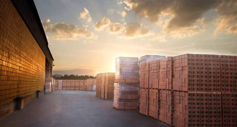 área externa de fábrica, com pilhas altas de blocos de cerâmica, cena iluminada com pôr do sol