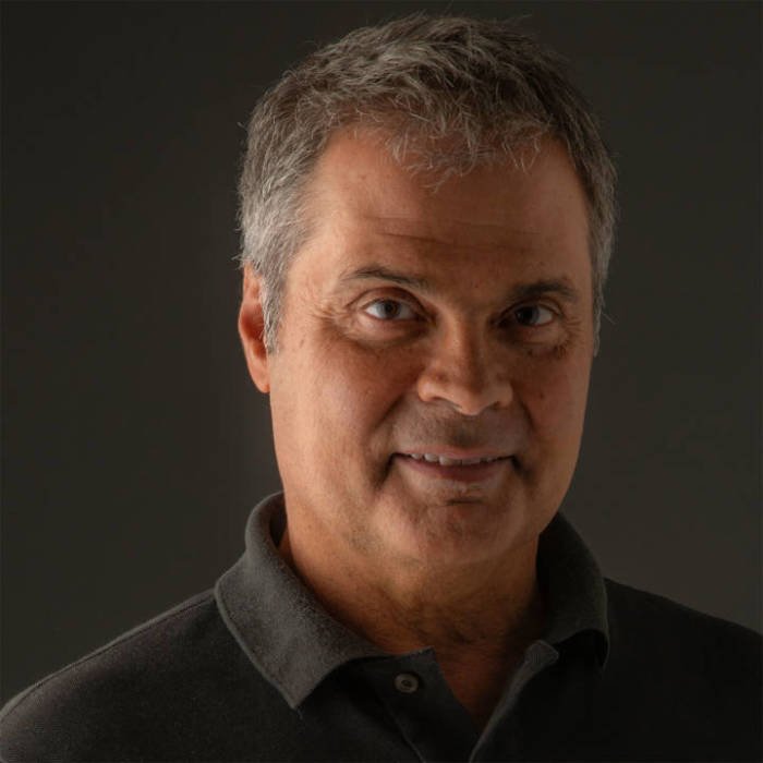fotografo-Mauricio_Cremonini.jpg homem de meia idade, com leve sorriso, de camisa polo preta em ambiente de fundo cinza, com luz dramática