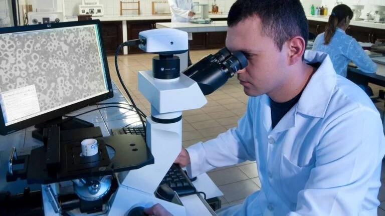 funcionário de jaleco analisando amostras em microscópio
