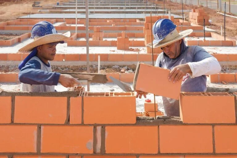 empreiteiros posicionando bloco para construção de parede