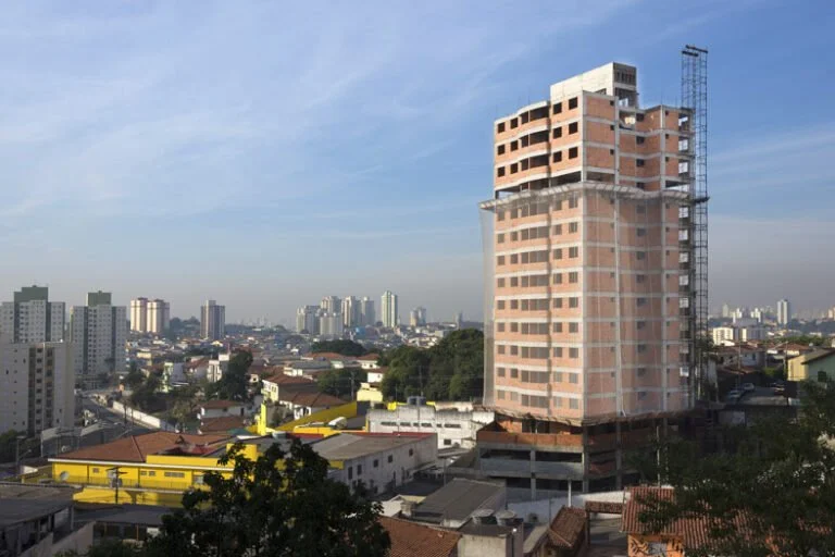 prédio em construção, com casas e demais prédios ao redor