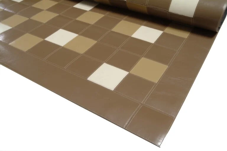tapete de couro marrom, uma parte enrolada e outra esticada, a parte não enrolada mostra o desenho feito pela costura semelhante a uma grade quadrículada, com alguns quadrados aleatoriamente preenchidos pelas cores branca, bege e marrom