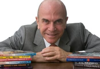 retrato profissional de homem de terceira idade, vestido com terno cinza e gravata, com alguns livros à sua frente