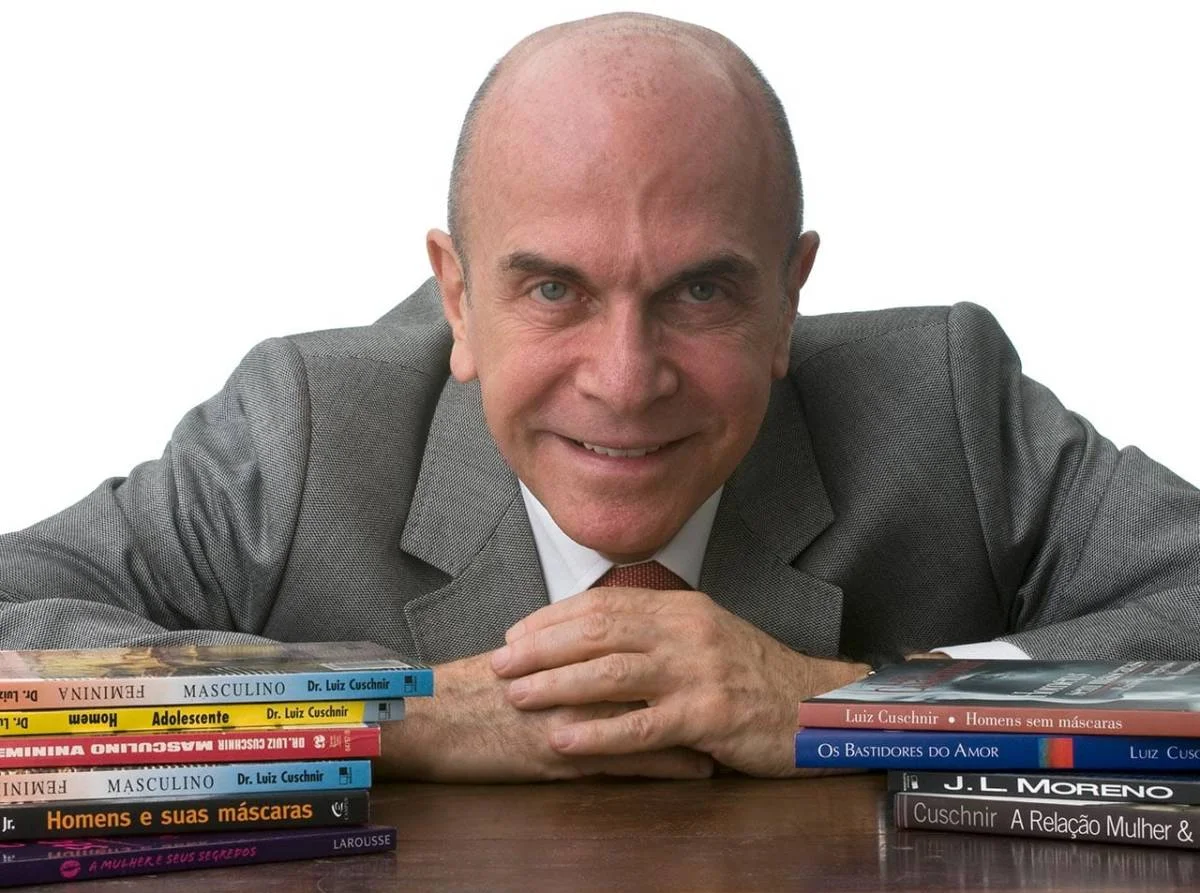 retrato profissional de homem de terceira idade, vestido com terno cinza e gravata, com alguns livros à sua frente