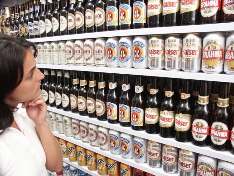 uma cliente observando prateleiras de supermercado com cervejas em latas e garrafas e alguns refrigerantes em latas expostos